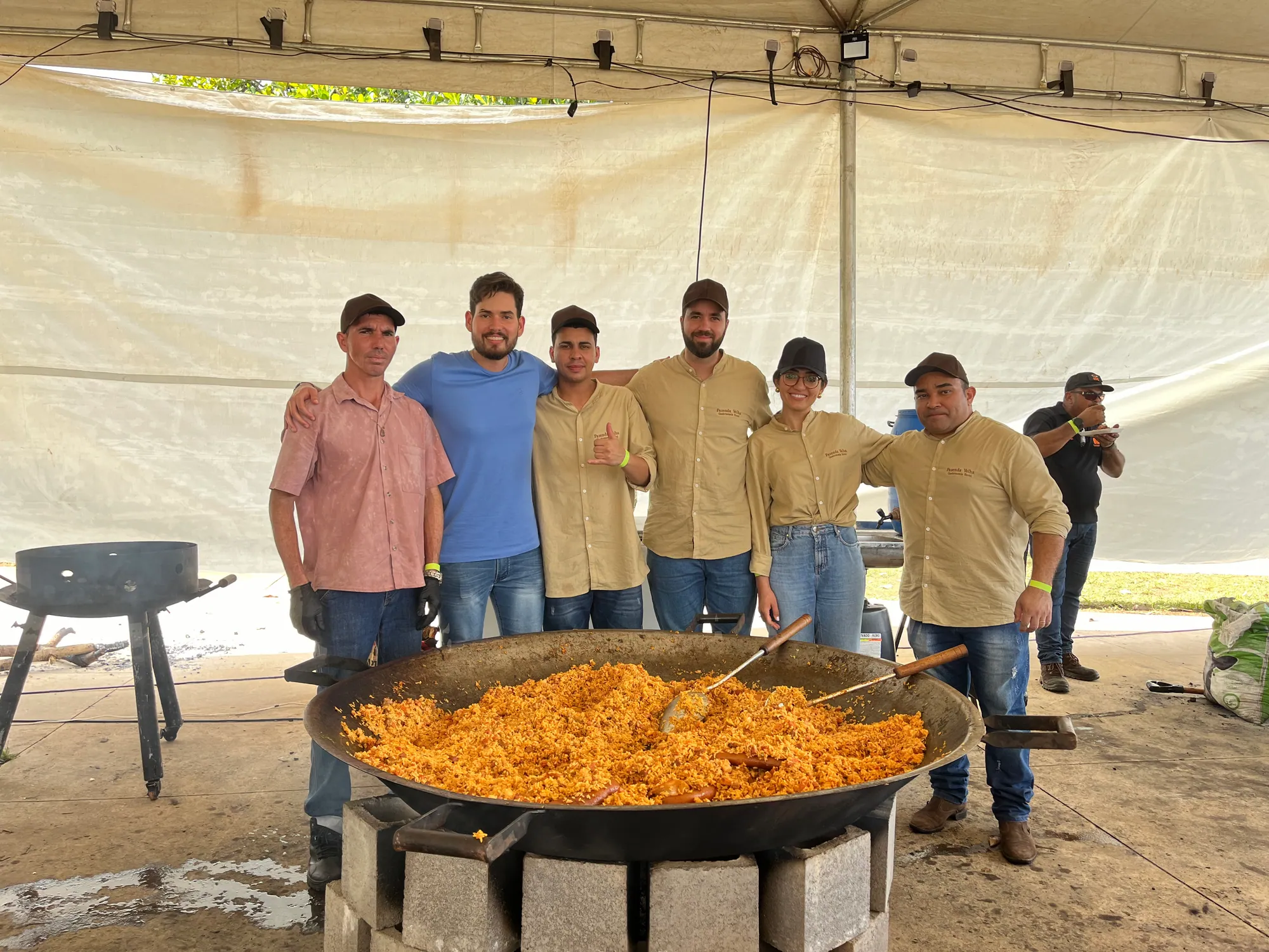 Equipe de cozinha diante de uma grande panela com um prato preparado durante o Ocidental Gastrô